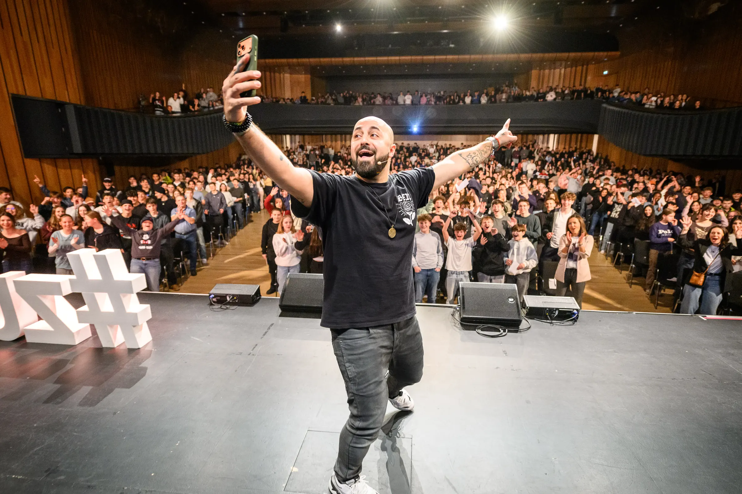Ali Mahlodji auf der Bühne, Selfie mit tausend Jugendlichen im Saal