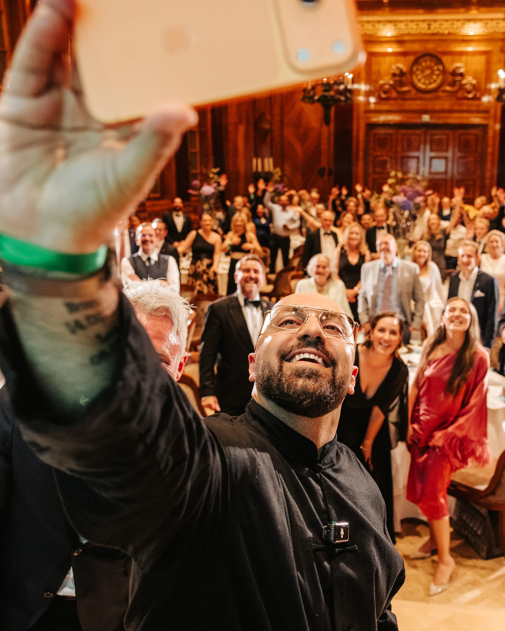 Ali Mahlodji laughing as he takes a selfie with the cheering audience of a festive hall
