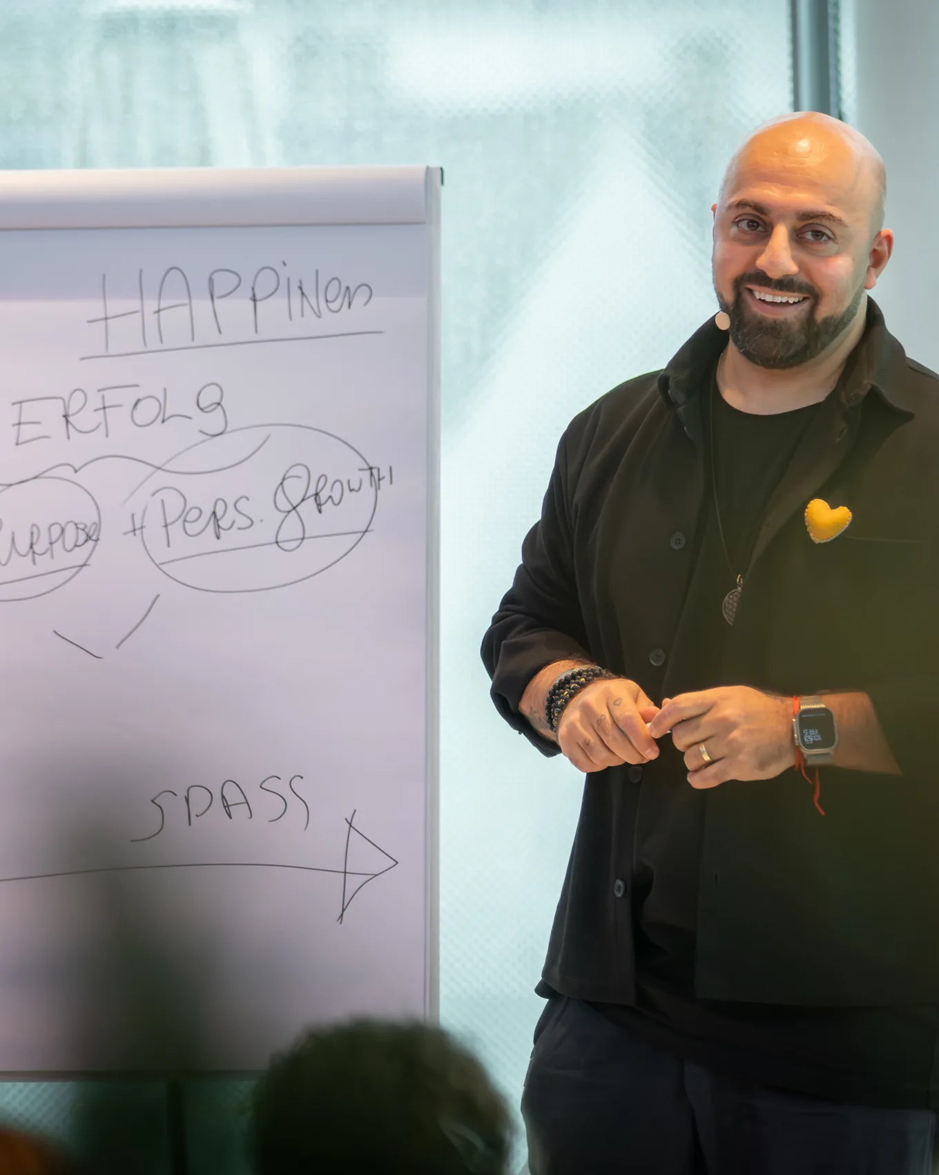 Ali Mahlodji smiling in front of a flipchart with handwritten notes on happiness and success