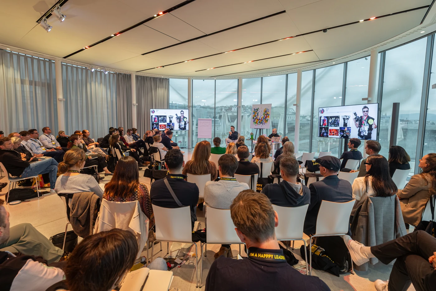 A full room with a glass façade at the Future Leadership Day 2025, participants listening to the conversation on stage