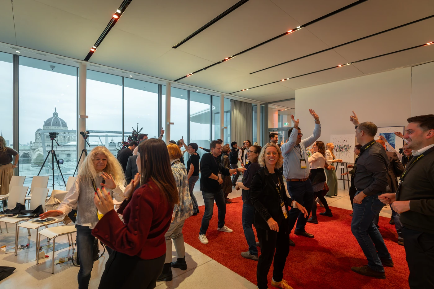 Dancing in daylight: participants laughing as they move on the red carpet, a view over Vienna through the glass façade behind them