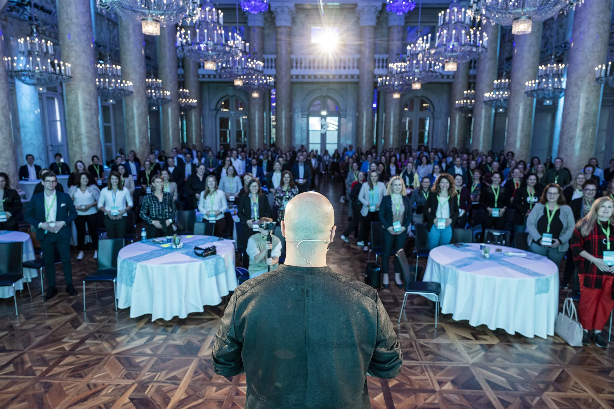 Ali Mahlodji from behind, facing a ballroom full of guests at round tables