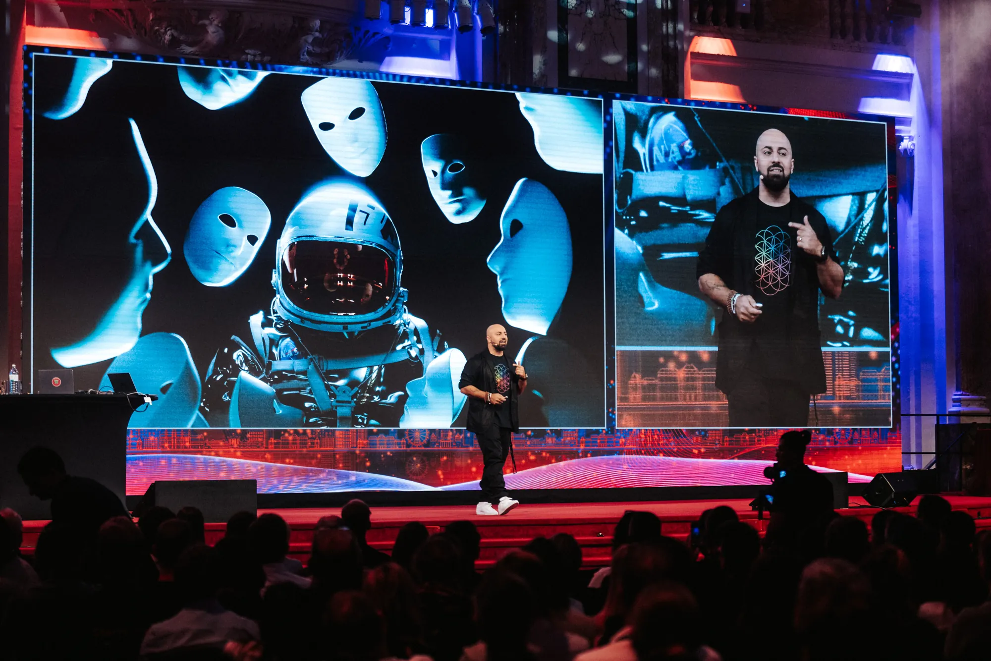 Ali Mahlodji on stage in front of a large LED wall with an astronaut motif