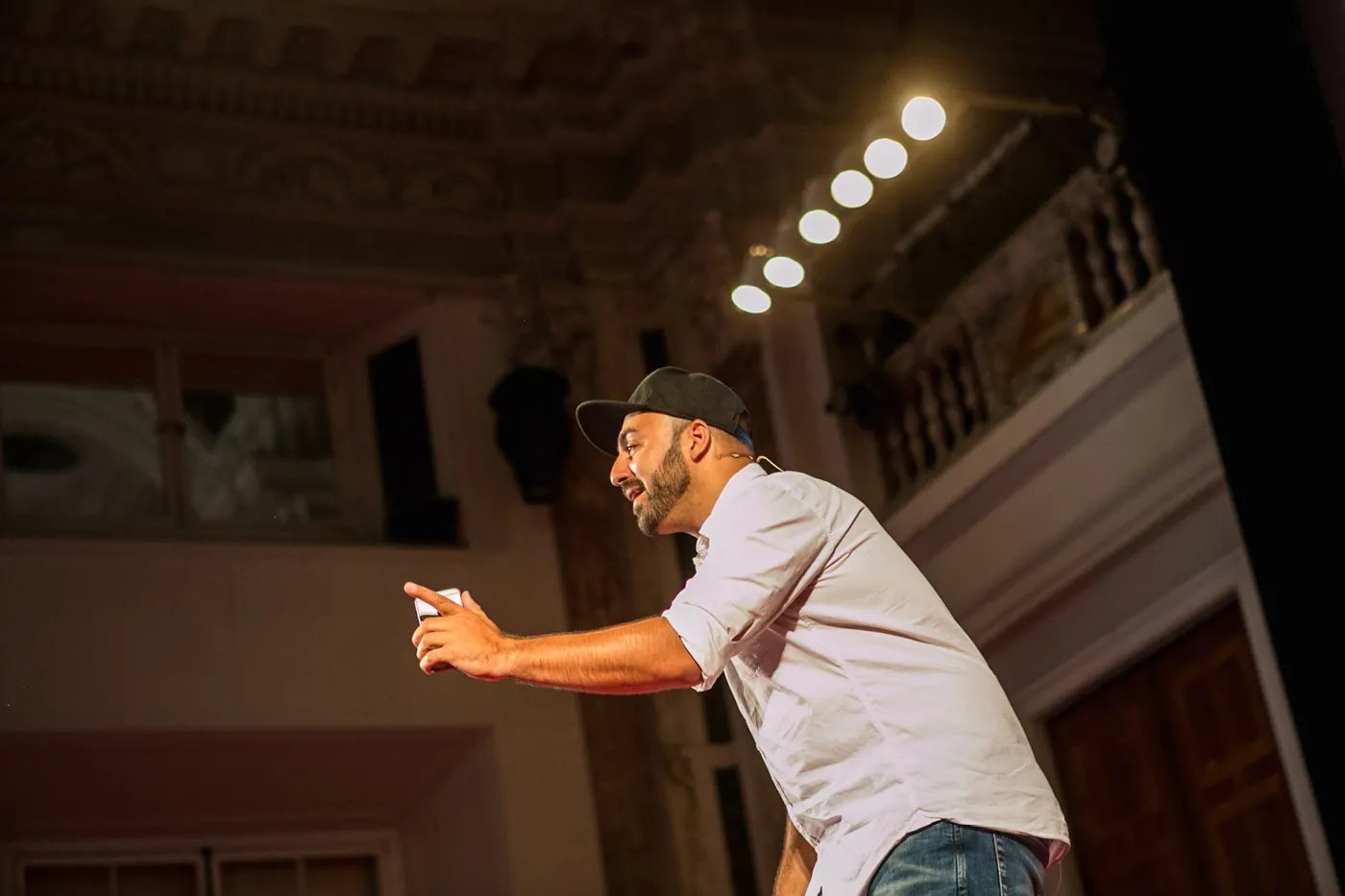 Ali Mahlodji wearing a cap, leaning forward in conversation with the audience