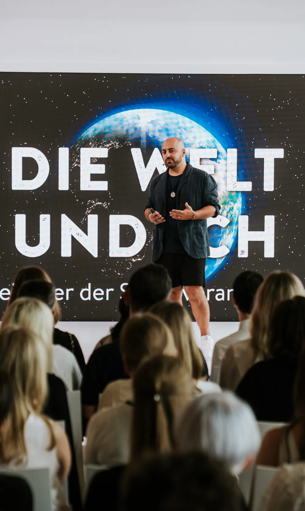 Ali Mahlodji in front of the screen “Die Welt und ich”