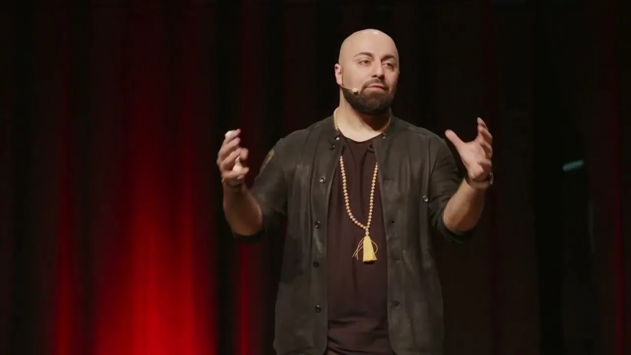 Ali Mahlodji with open hands in front of a red stage curtain