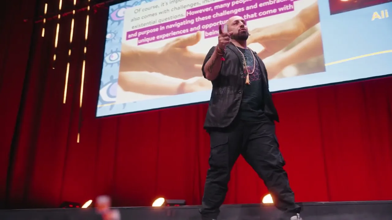 Ali Mahlodji on stage in front of a screen, index finger raised