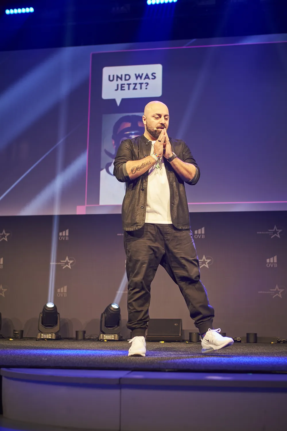 Ali Mahlodji with folded hands in front of the slide “Und was jetzt?”