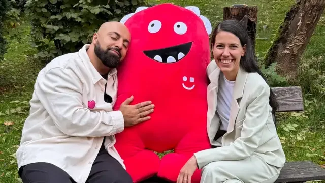 Anna und Ali Mahlodji mit einem roten Plüschmaskottchen im Garten, Standbild aus Folge 33