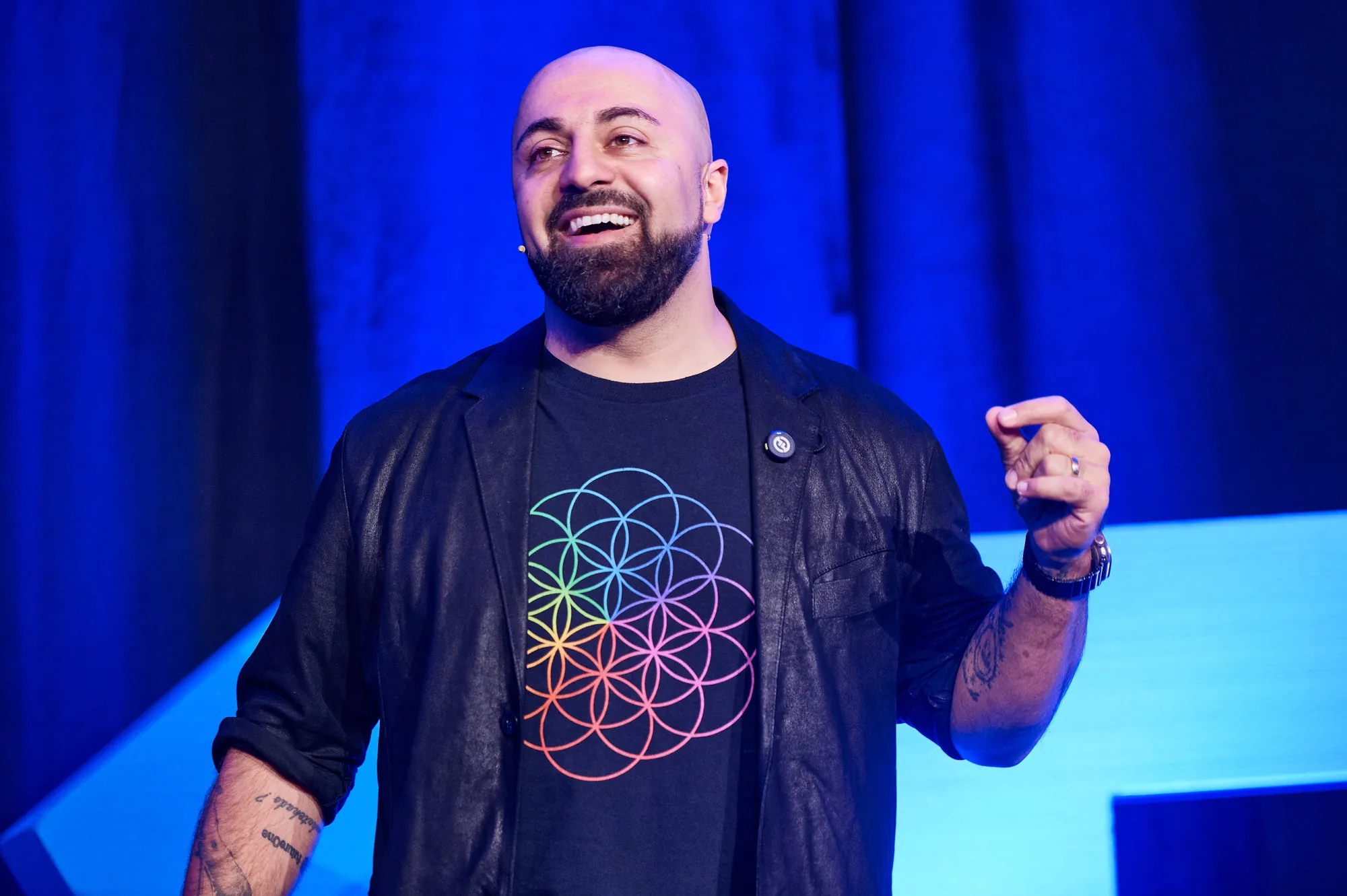 Ali Mahlodji lachend auf einer blau beleuchteten Bühne, mitten in der Keynote