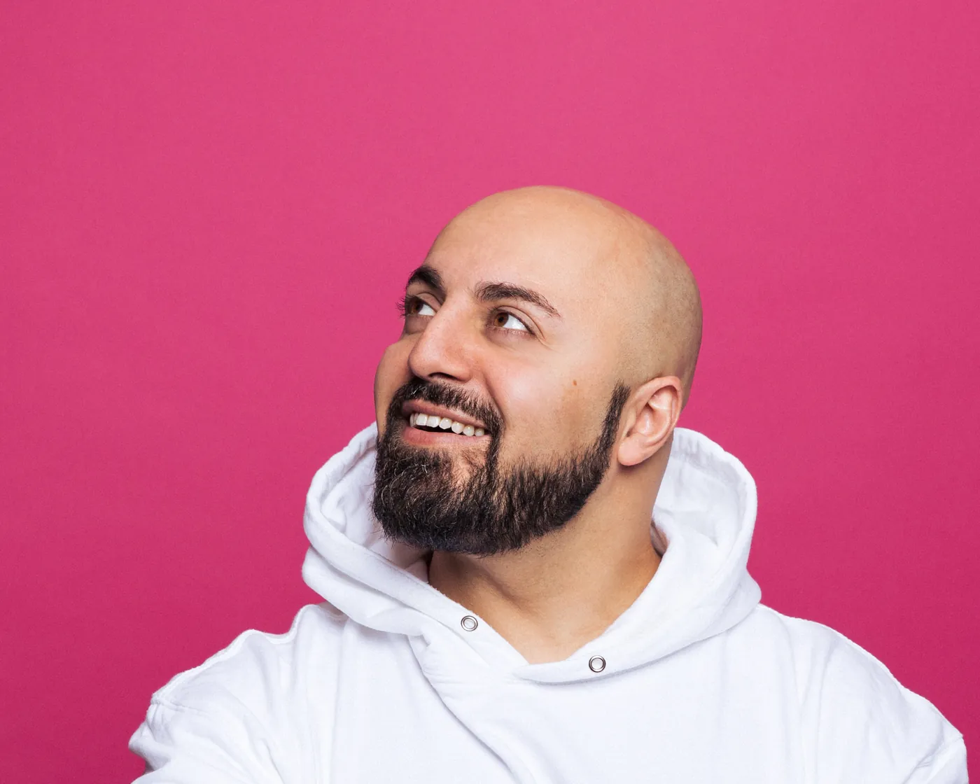 Ali Mahlodji im Studio vor pinkem Hintergrund, lächelnd mit Blick nach oben